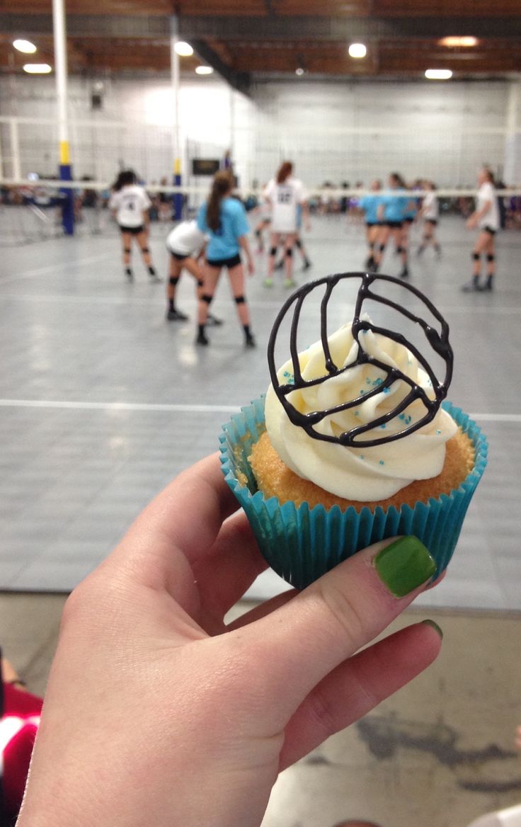 a person holding up a cupcake with white frosting and sprinkles