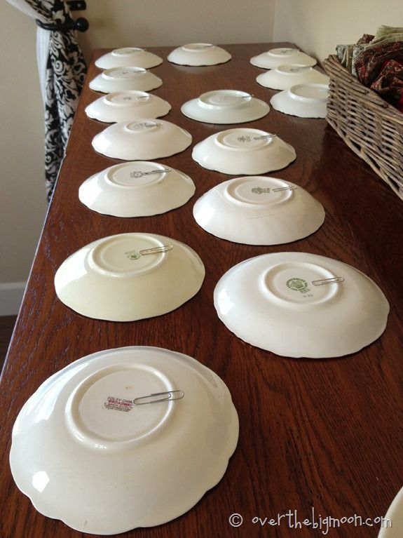 white plates are lined up on a long wooden table in front of a basket full of pine cones