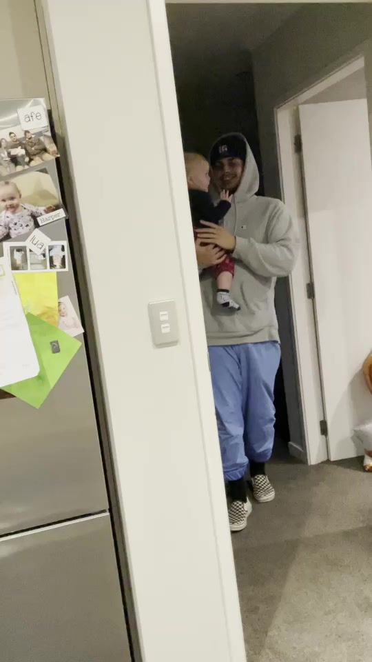 a man holding a baby in his arms while standing next to a refrigerator freezer