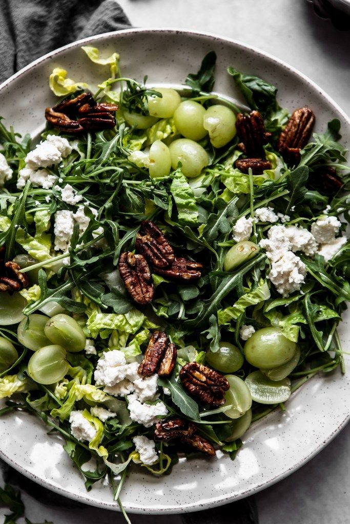 a salad with grapes, pecans and goat cheese in a white bowl on a table