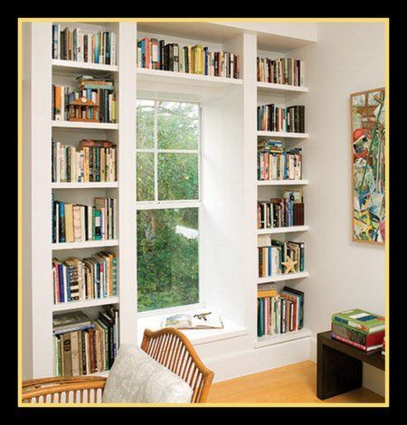 a living room filled with lots of books on top of white shelving units next to a window