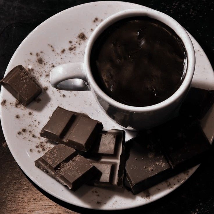 a white plate topped with pieces of chocolate next to a cup of coffee and spoon