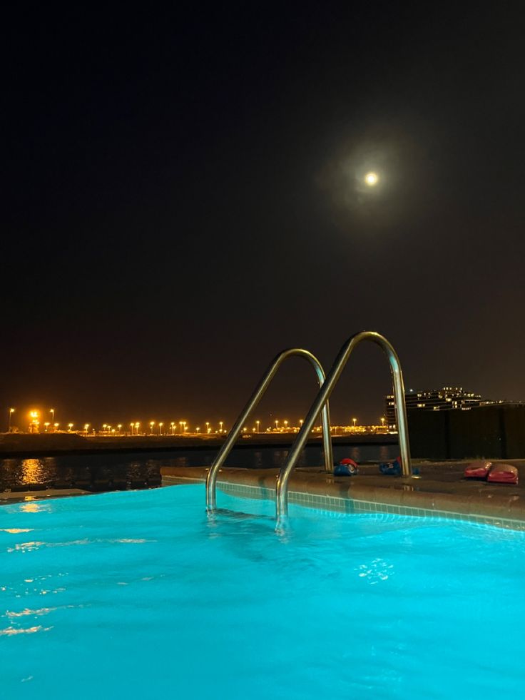 an empty swimming pool at night with the moon in the sky and lights reflecting on the water