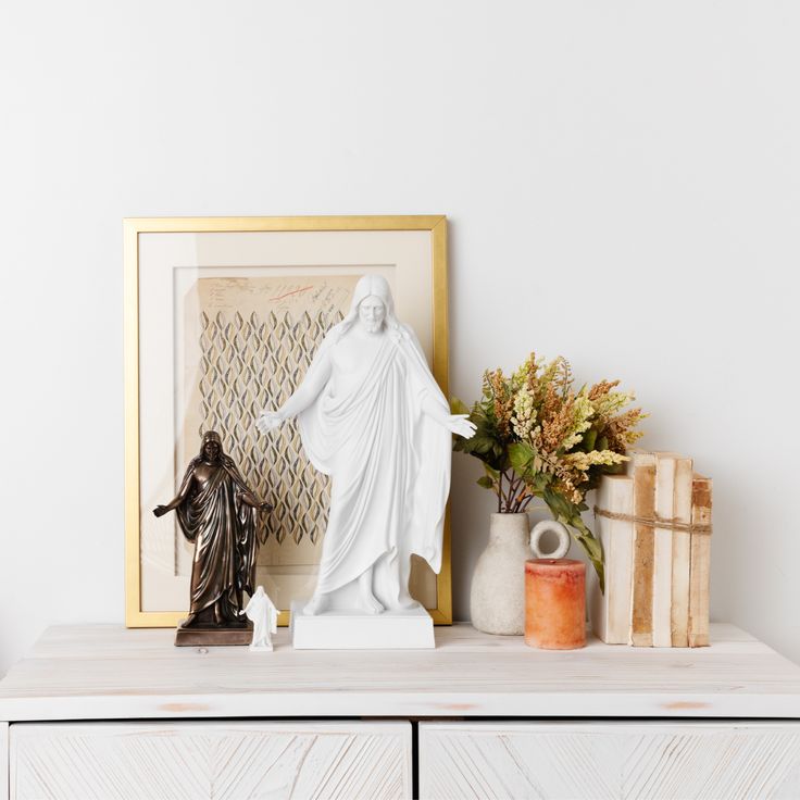 a white statue sitting on top of a wooden dresser next to a vase with flowers