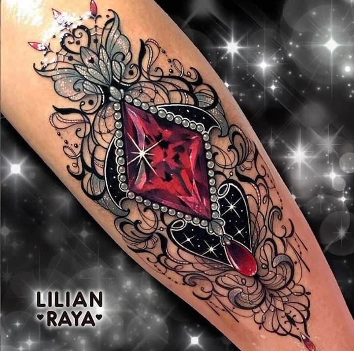 a woman's leg with an ornate tattoo design and red stone in the center