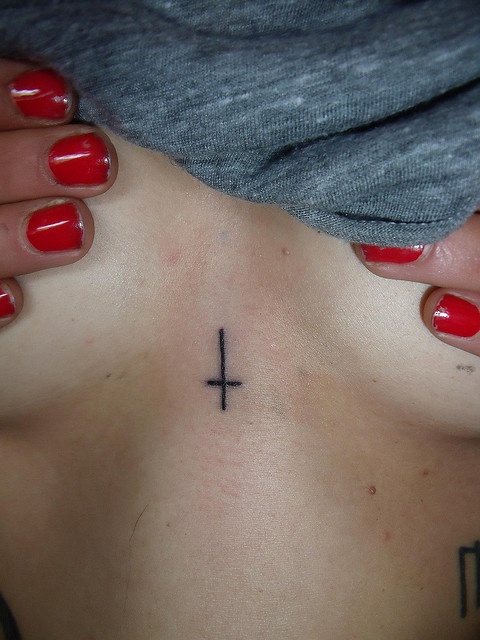 a woman's chest with a cross tattoo on it and red nail polishes