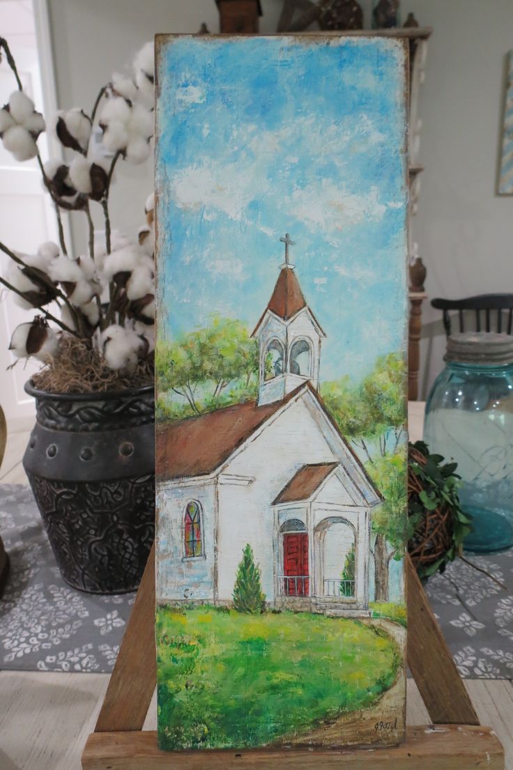 an easel with a painting of a church on it and flowers in the background