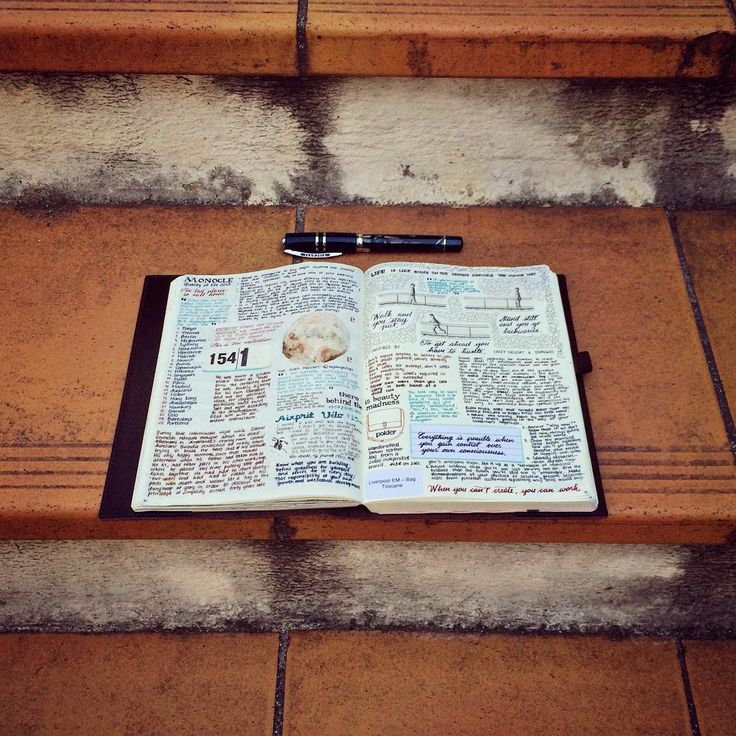 an open book sitting on top of a wooden bench next to a pen and paper