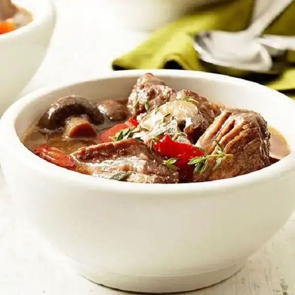 two bowls filled with meat and vegetables on top of a white countertop next to silverware