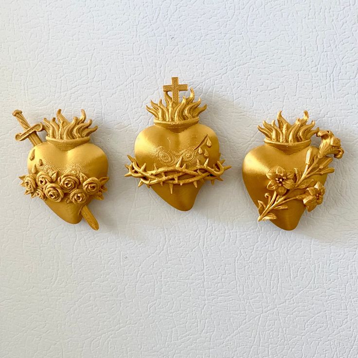 three gold heart shaped ornaments on a white wall