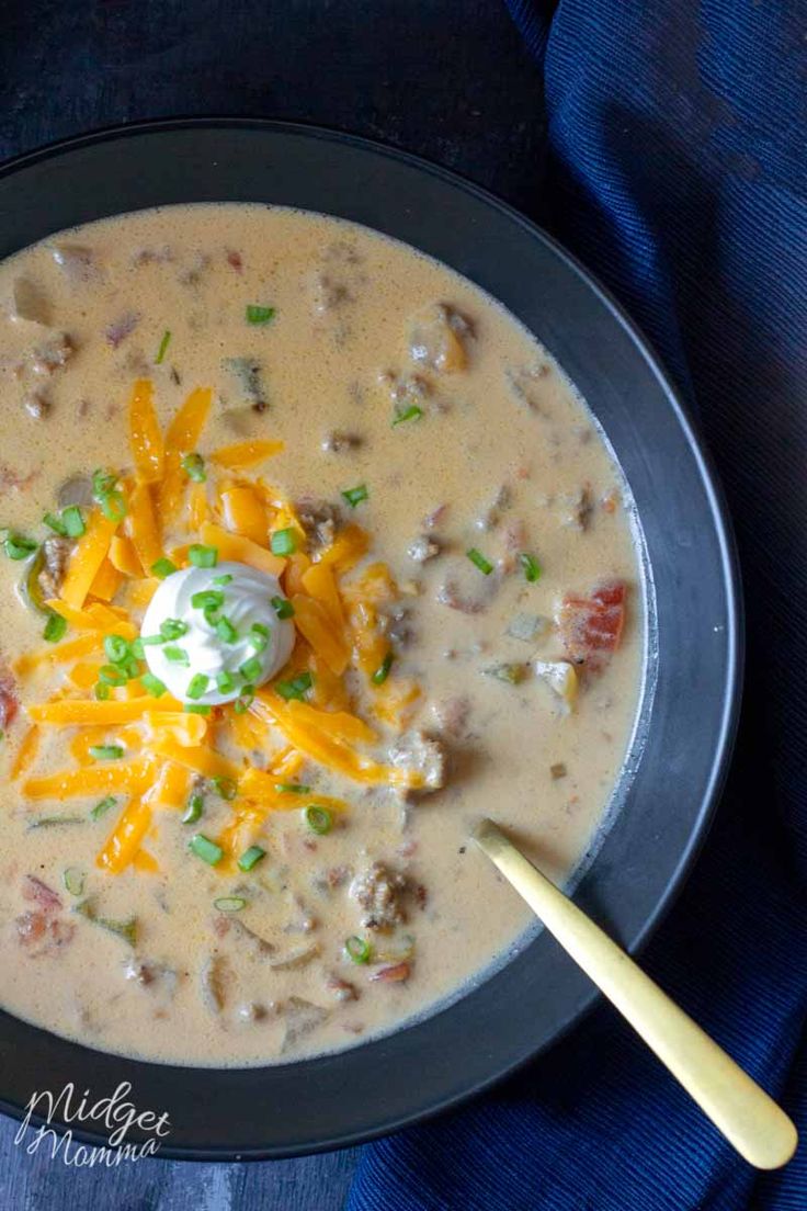 a bowl of soup with cheese and sour cream in it on a blue cloth next to a wooden spoon