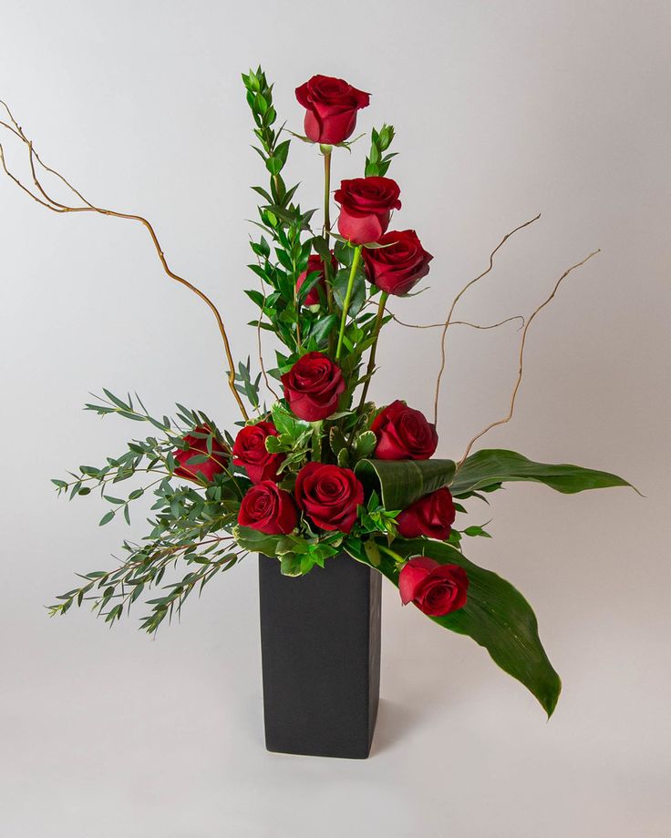 a black vase filled with red roses and greenery