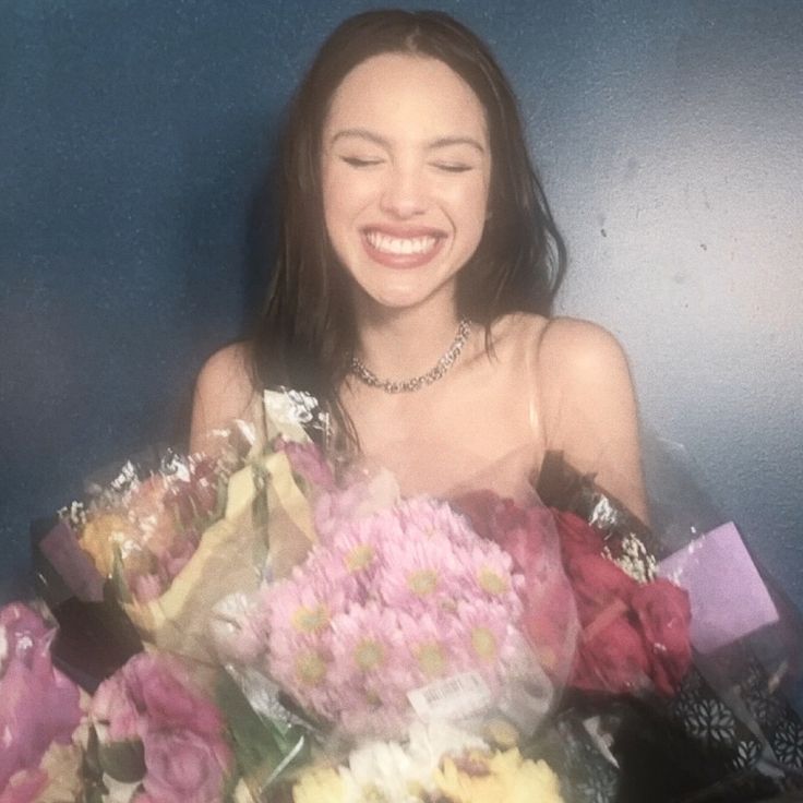 a woman holding flowers in her hands and smiling at the camera while she is surrounded by other flowers