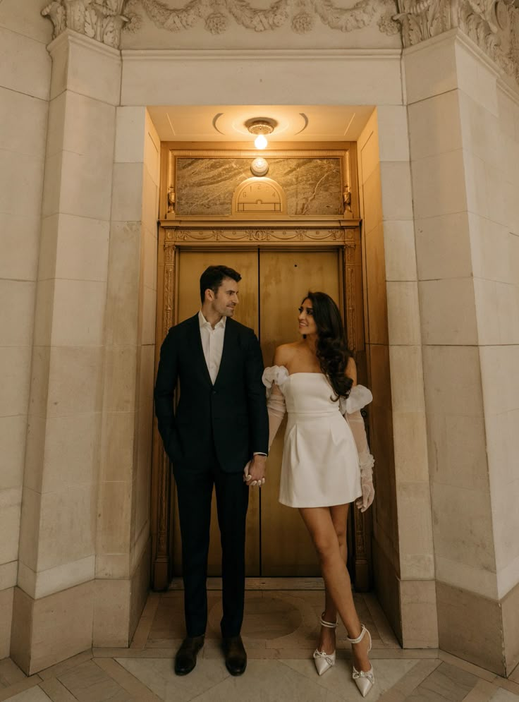 a man and woman standing in front of an entrance to a building with marble columns