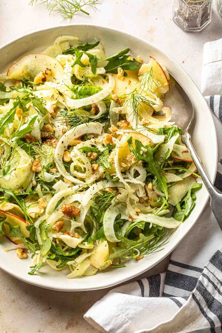 a white bowl filled with salad on top of a table next to utensils