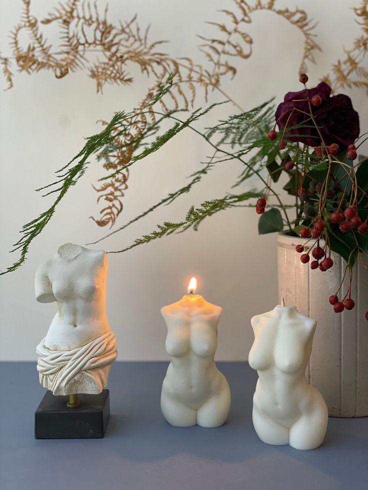 two white candles sitting on top of a table next to a vase filled with flowers