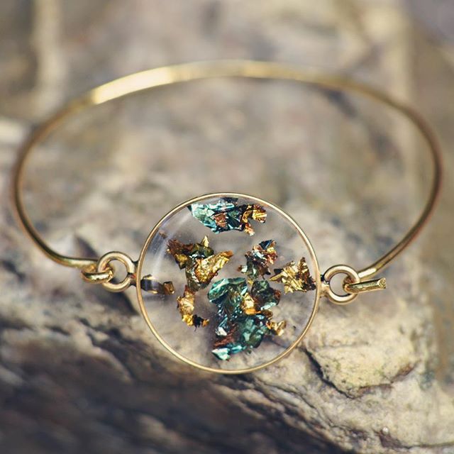 a close up of a gold bracelet on a rock with flowers in the center and leaves around it