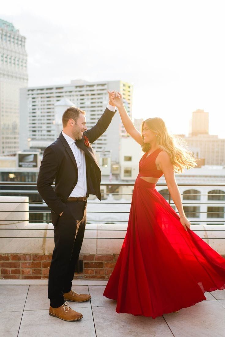 a man and woman in formal wear dancing on the roof of a building with skyscrapers in the background