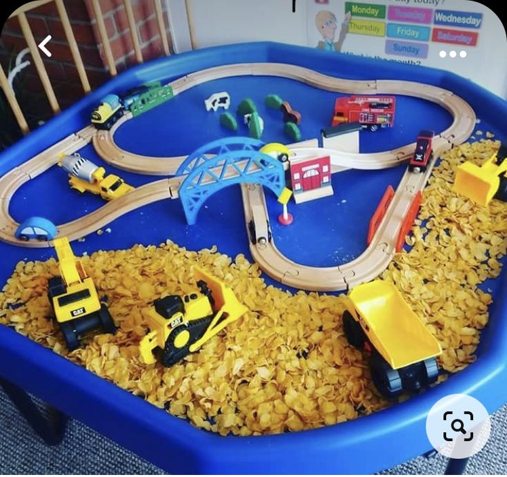 a toy train set in a blue plastic container with yellow toys on the tracks and construction vehicles