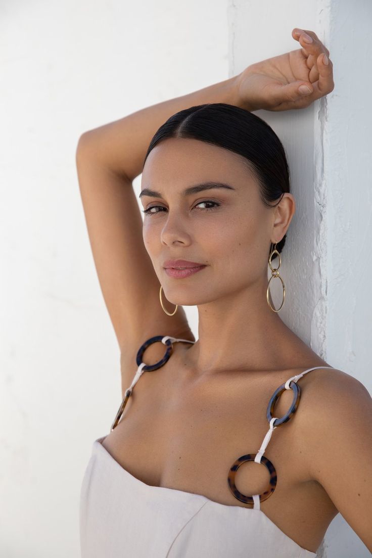 a beautiful woman leaning against a wall with her hands on her head and wearing large hoop earrings