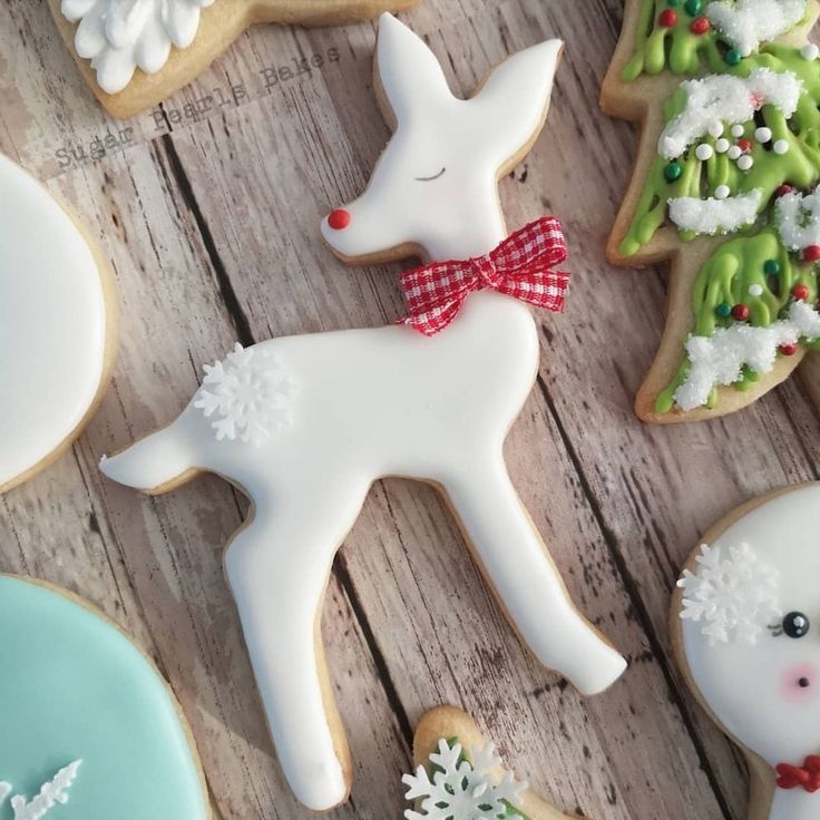 decorated christmas cookies on a wooden table with snowflakes and deers in the background