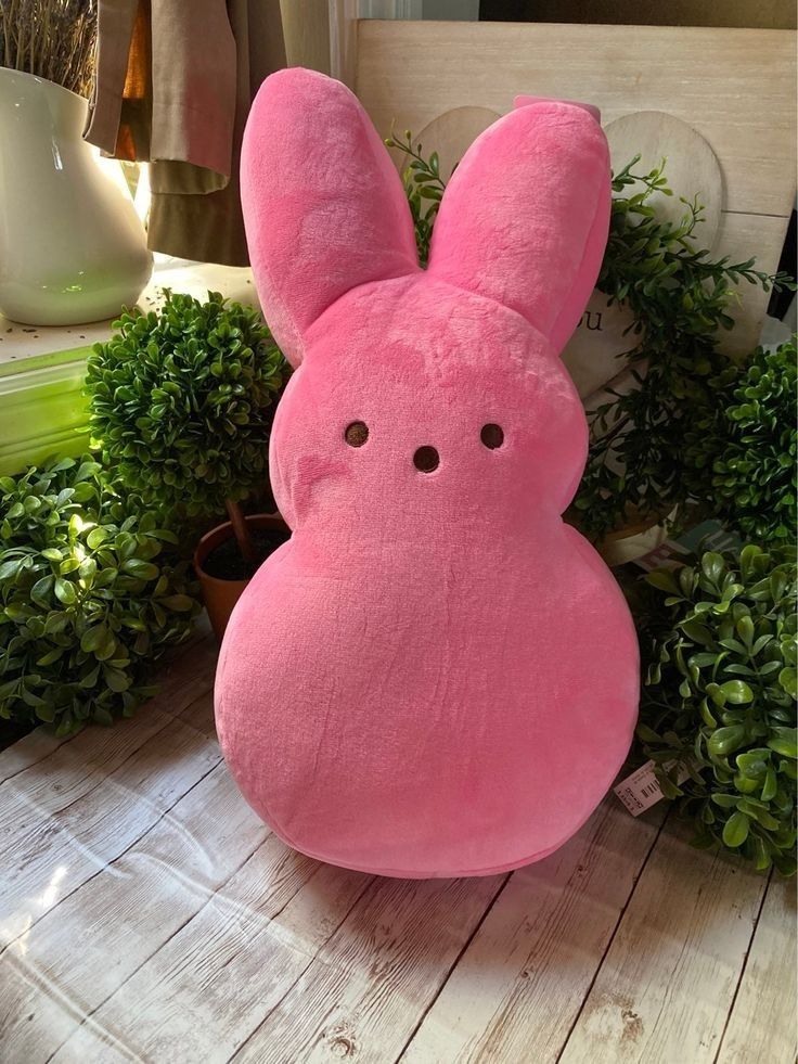 a pink bunny stuffed animal sitting on top of a wooden floor next to green plants