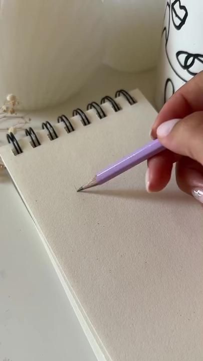 a person holding a pencil in their left hand and writing on a notepad next to a coffee mug