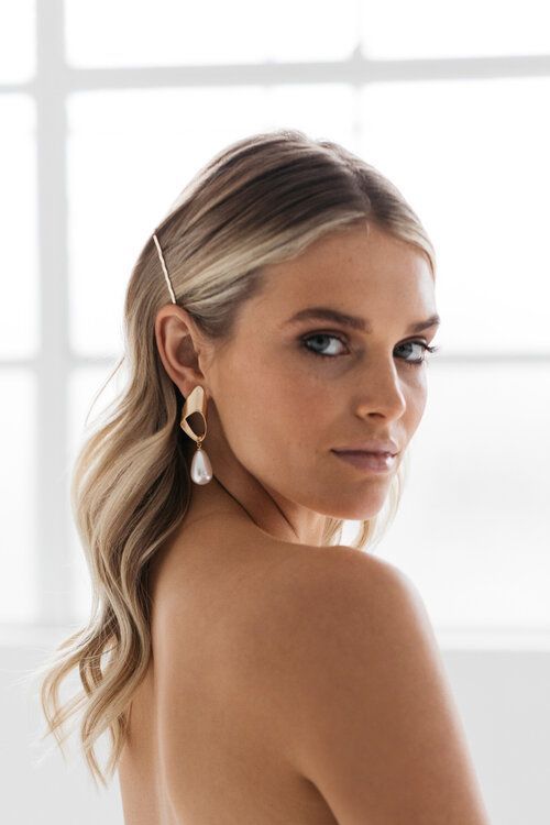 a woman with long blonde hair wearing large gold hoop earrings and a white dress is looking off to the side