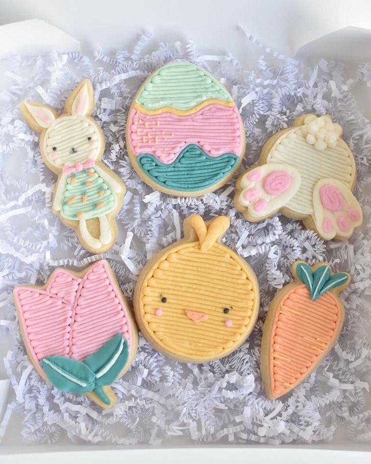 four decorated cookies in a box with white lace on the top and one has a bunny, carrots, and an egg