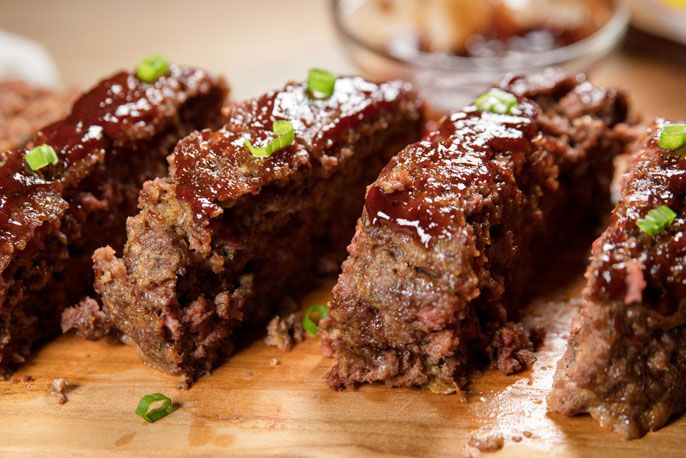 meatloaf with green onions and ketchup on a cutting board