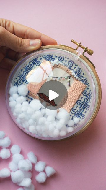 a person is holding a needle case with cotton balls in it on a pink surface