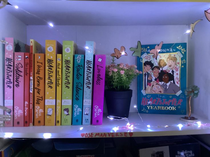 there are many books on the shelf with fairy lights around them and a potted plant next to it