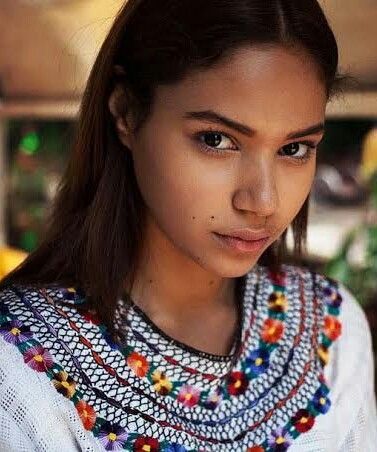 a young woman with long hair wearing a colorful necklace and looking off to the side