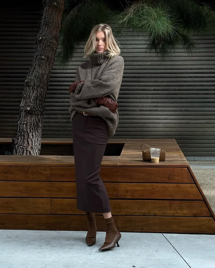 a woman standing in front of a wooden bench with her arms crossed and looking at the camera