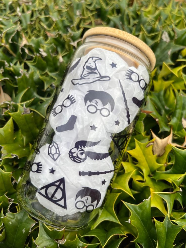 a glass jar with harry potter stickers on it sitting in the grass next to leaves