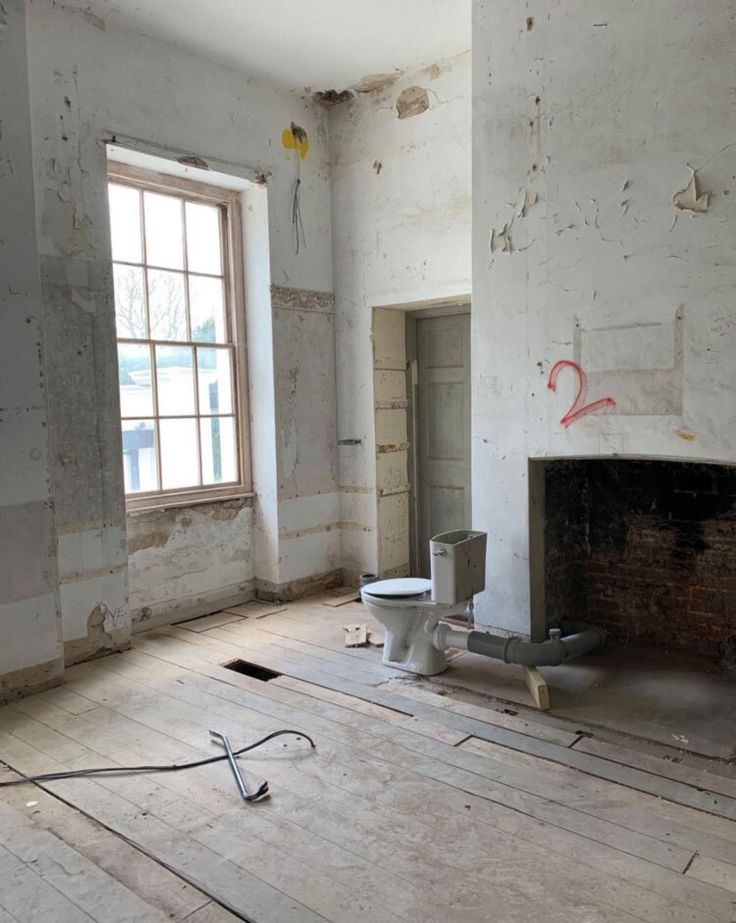 an unfinished room with a fireplace and two toilets on the floor in front of a window