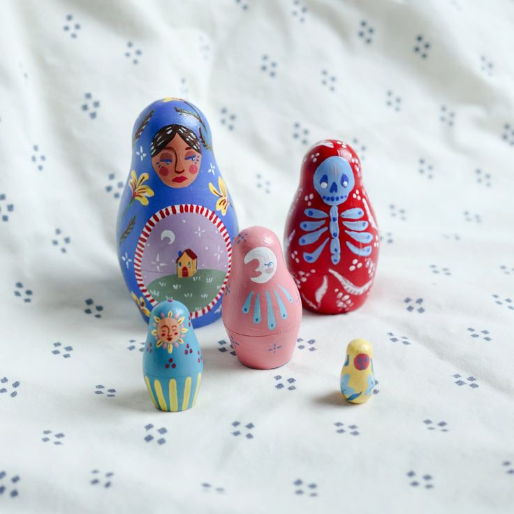 three colorful nesting dolls sitting on top of a white bed sheet next to each other