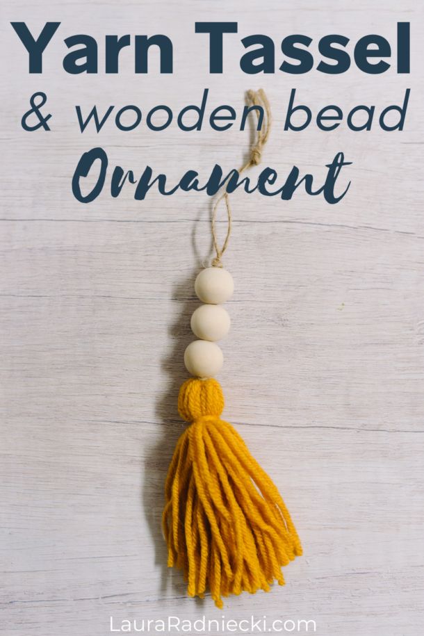 yarn tassel and wooden bead ornament hanging on white wood with text overlay