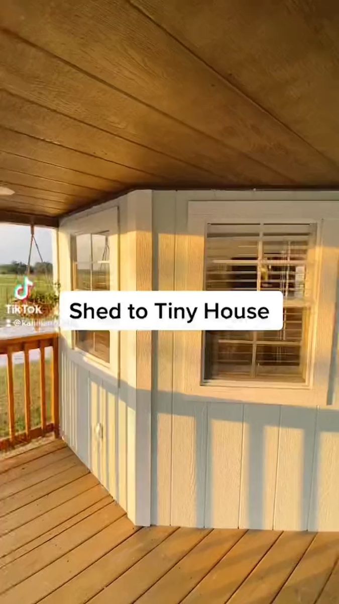 the front porch of a tiny house with wood floors and white sidings, has an open door that says shed to tiny house