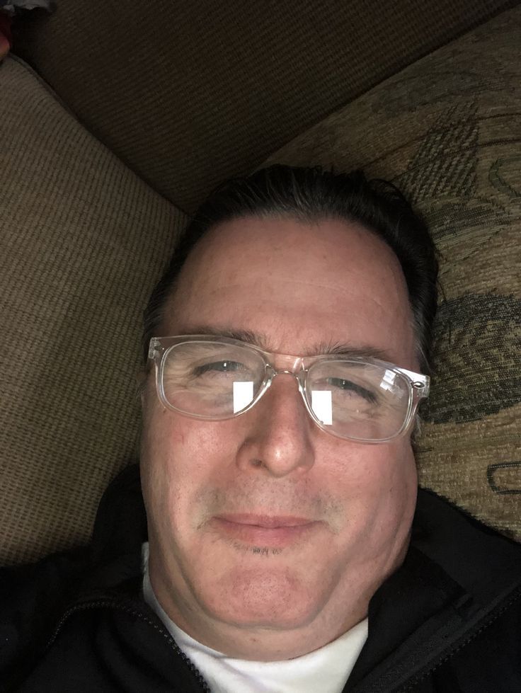 a man wearing glasses and a black jacket is sitting on a couch with his head turned to the side