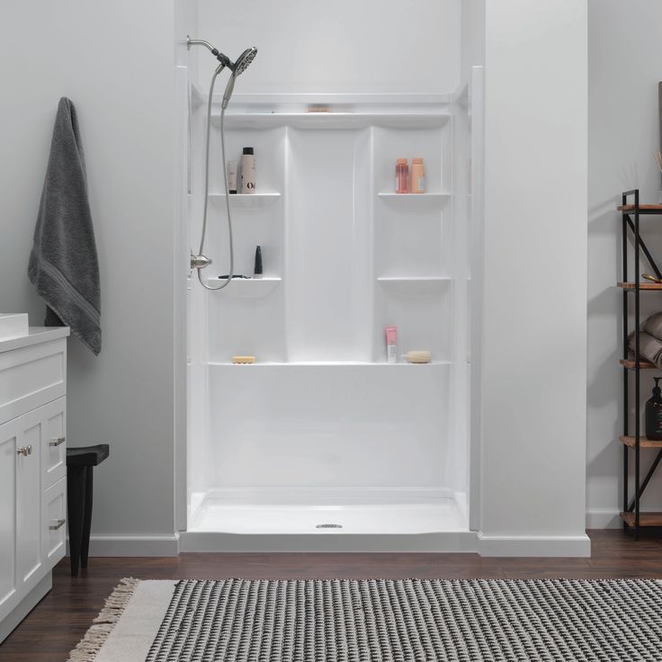 a bathroom with white walls and flooring, including a shower stall that has shelves on the wall