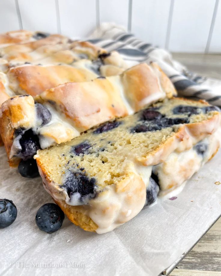 a loaf of blueberry bread sitting on top of a piece of parchment paper next to fresh blueberries