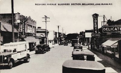 an old black and white photo of cars driving down the street in front of businesses