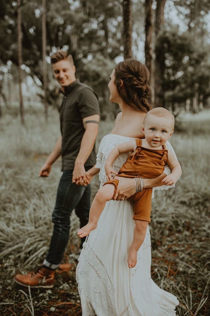 a man and woman holding a baby in the woods