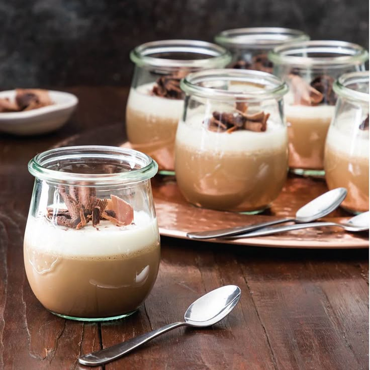 there are many desserts in glass jars on the table with spoons next to them