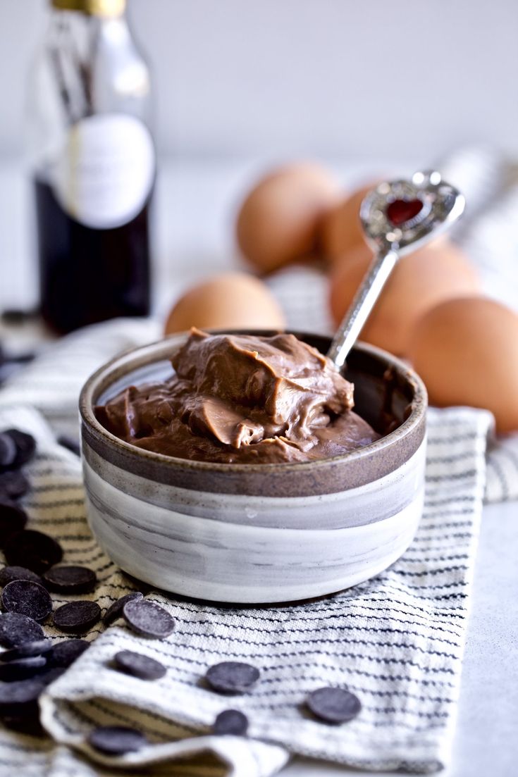 a bowl filled with chocolate pudding next to eggs and a bottle of wine on a table