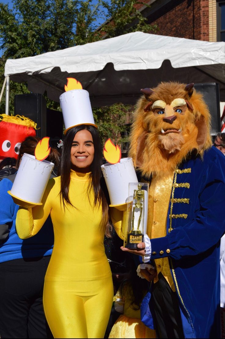 a woman in a yellow dress and lion costume holding two beer mugs while standing next to a man in a blue suit