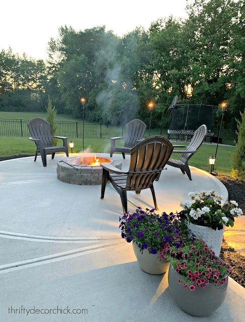 an outdoor fire pit surrounded by chairs and potted plants with lit candles in the background