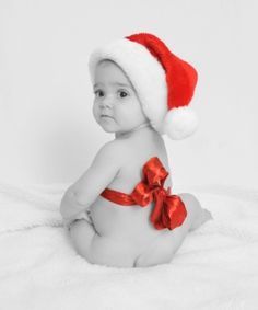 a baby wearing a santa hat and sitting on a white blanket with a red ribbon