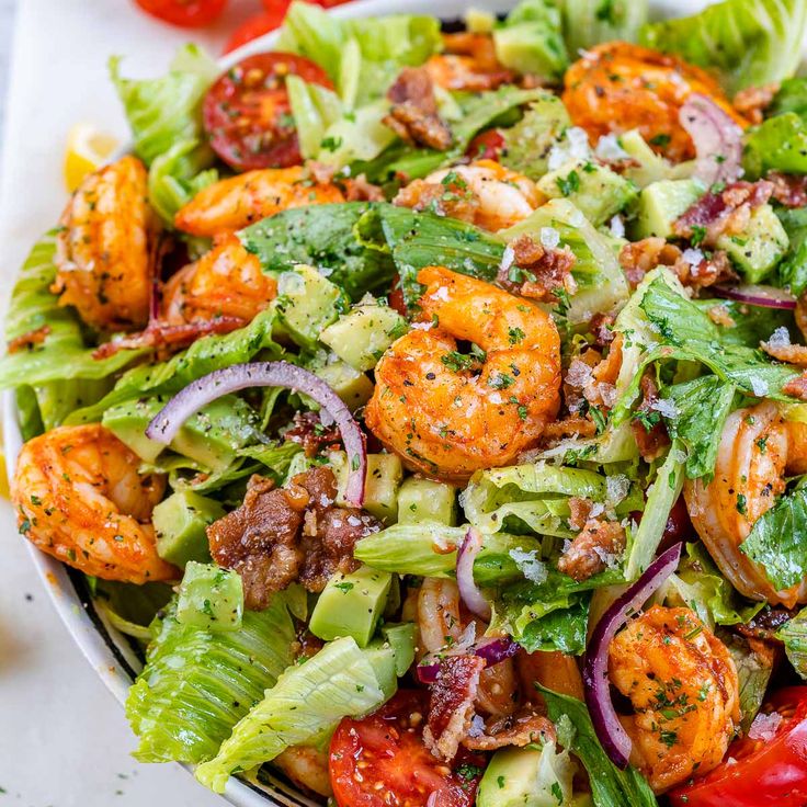 a salad with shrimp, lettuce, tomatoes and onions in a white bowl